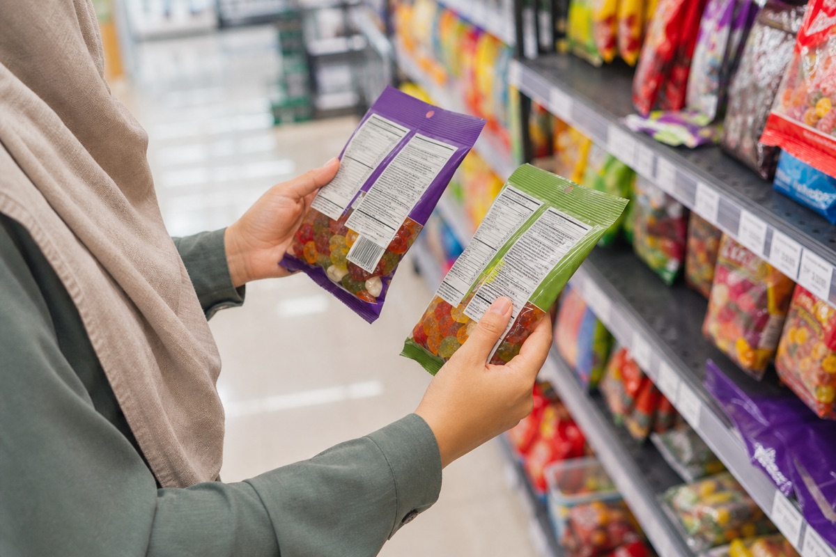 Shopper comparing the back labels of two unbranded gummy candy bags in a grocery aisle.